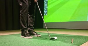A young man carefully lining up a virtual golf shot with his putter while using his in-home golf simulator system.