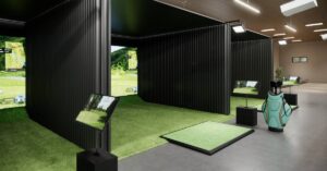 The interior of an indoor golf simulator facility that includes three golf simulators separated by blackout walls.