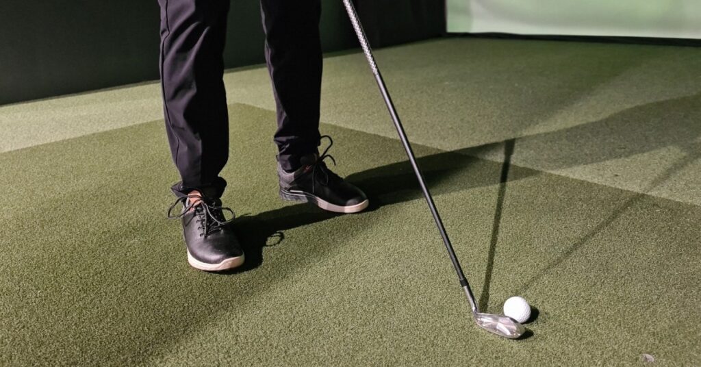 A young golfing enthusiast lining up their putting shot while aiming towards a virtual golfing simulator.